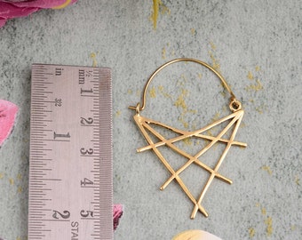Peut inclure: Boucles d'oreilles géométriques dorées avec un motif en forme d'étoile. Les boucles d'oreilles mesurent environ 3,8 cm de long. Elles sont présentées sur une surface vert clair avec des motifs floraux.