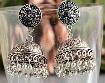 May include: Silver dangle earrings with a floral design and a bell-shaped bottom. The earrings have a silver chain and a silver bead drop.