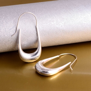 Puede incluir: Un par de pendientes de aro de plata con un diseño curvo único. Los pendientes son simples y elegantes, y serían una gran adición a cualquier colección de joyas.