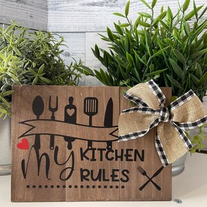 May include: Wooden sign with the text "My Kitchen Rules" in black lettering. The sign is decorated with a black and white checkered bow and a row of kitchen utensils in black.