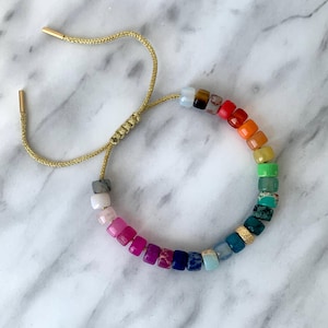 May include: A rainbow gemstone bracelet with a gold adjustable cord. The bracelet features a variety of colorful square-shaped gemstones.