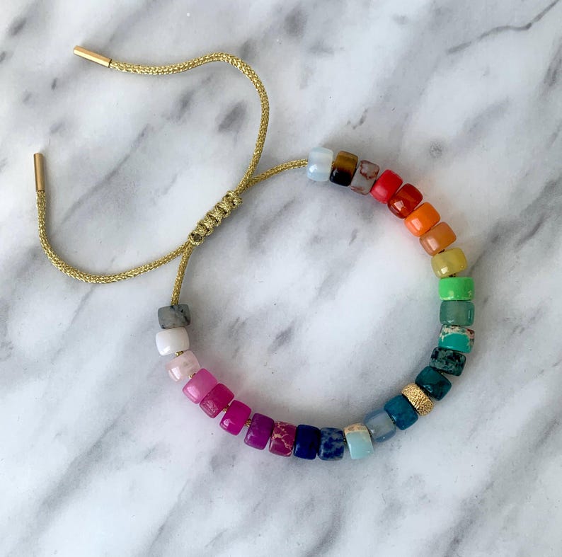 May include: A rainbow gemstone bracelet with a gold adjustable cord. The bracelet features a variety of colorful square-shaped gemstones.