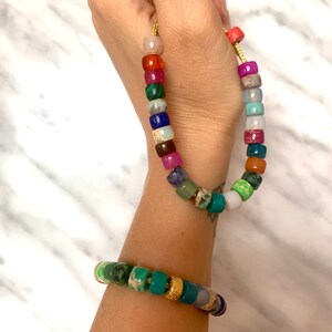 May include: A colorful beaded necklace and bracelet made of various gemstones, including green, blue, red, and pink. The necklace and bracelet are both strung on a gold cord.