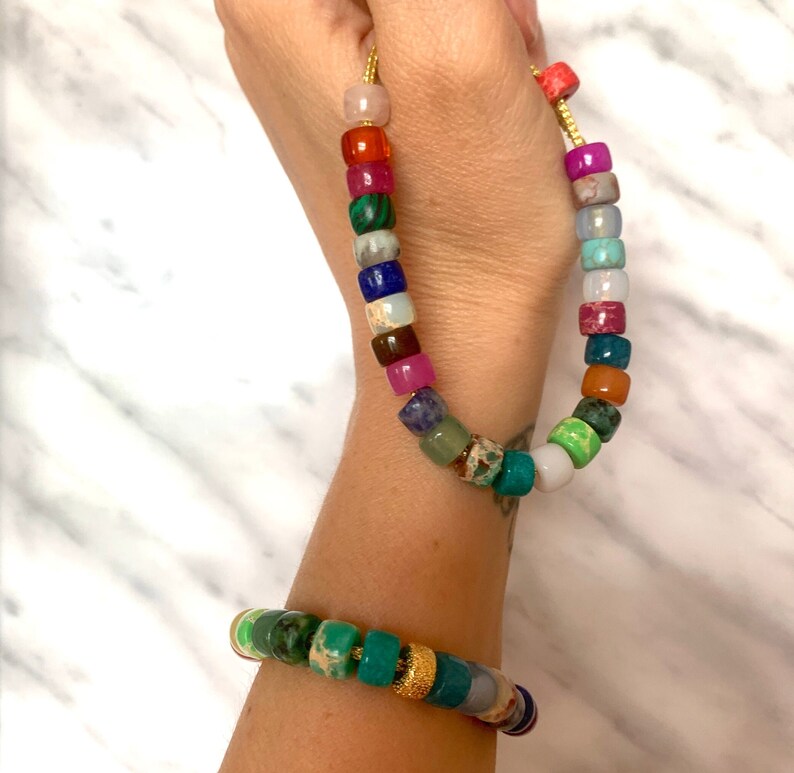 May include: A colorful beaded necklace and bracelet made of various gemstones, including green, blue, red, and pink. The necklace and bracelet are both strung on a gold cord.