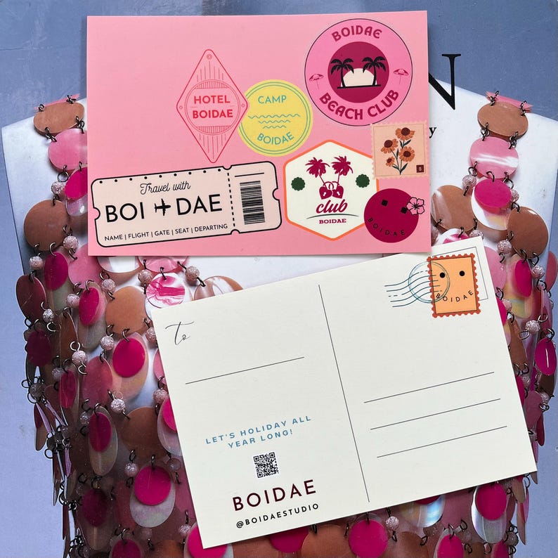 Pode incluir: Um postal cor-de-rosa com autocolantes de viagem como Hotel Boidae, Camp Boidae e um log&oacute;tipo Boidae Beach Club, juntamente com um bilhete Travel with Boidae. Por baixo, um postal creme exibe um selo, um c&oacute;digo QR e o texto Let's Holiday All Year Long, Boidae e @boidaestudio.