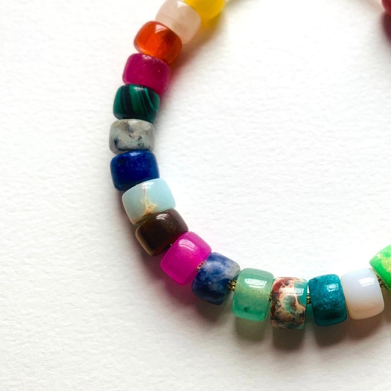May include: A colorful beaded bracelet with a rainbow of colors, including red, orange, yellow, green, blue, indigo, and violet. The beads are made of different types of stones, such as agate, amethyst, and jasper.