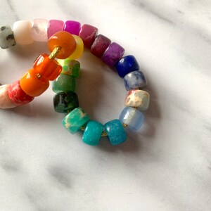May include: A rainbow colored beaded bracelet made of various gemstones. The bracelet is made of small, square-shaped beads.