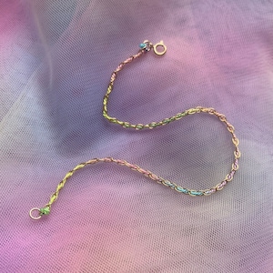 May include: A delicate gold chain bracelet with a multi-colored design. The chain is made of small, linked ovals with alternating colors of pink, green, and blue.