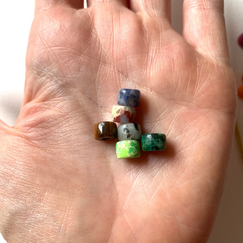 May include: A collection of six small, round, colorful gemstone beads. The beads are made of various types of stone, including tiger's eye, jasper, and turquoise.