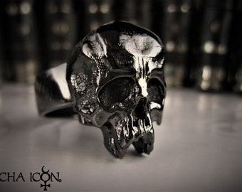 May include: A black skull ring with a detailed design. The ring is made of metal and has a polished finish.