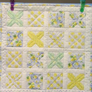 May include: A yellow and white quilt with a lemon print. The quilt is made up of 12 squares, each with a different pattern. The quilt is edged with a white border.