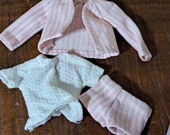 May include: A pink and white striped cardigan, a white knit shirt, and pink and white striped shorts. The clothing is made of a soft, knitted fabric.