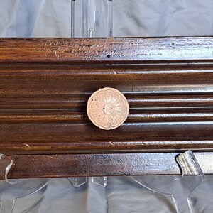 May include: A dark brown wooden wall mounted shelf with three white ceramic knobs with pink floral designs.