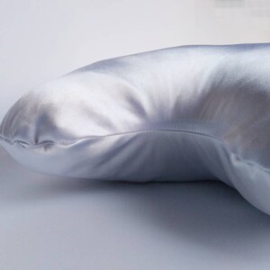 以下が含まれることがあります： 湾曲した形の白いサテンの枕。枕は柔らかく滑らかで、睡眠や休息に最適です。