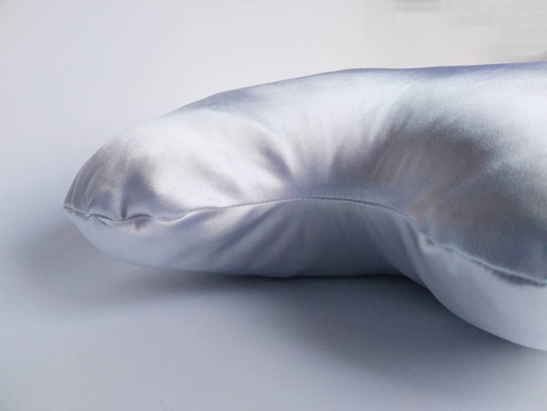以下が含まれることがあります： 湾曲した形の白いサテンの枕。枕は柔らかく滑らかで、睡眠や休息に最適です。