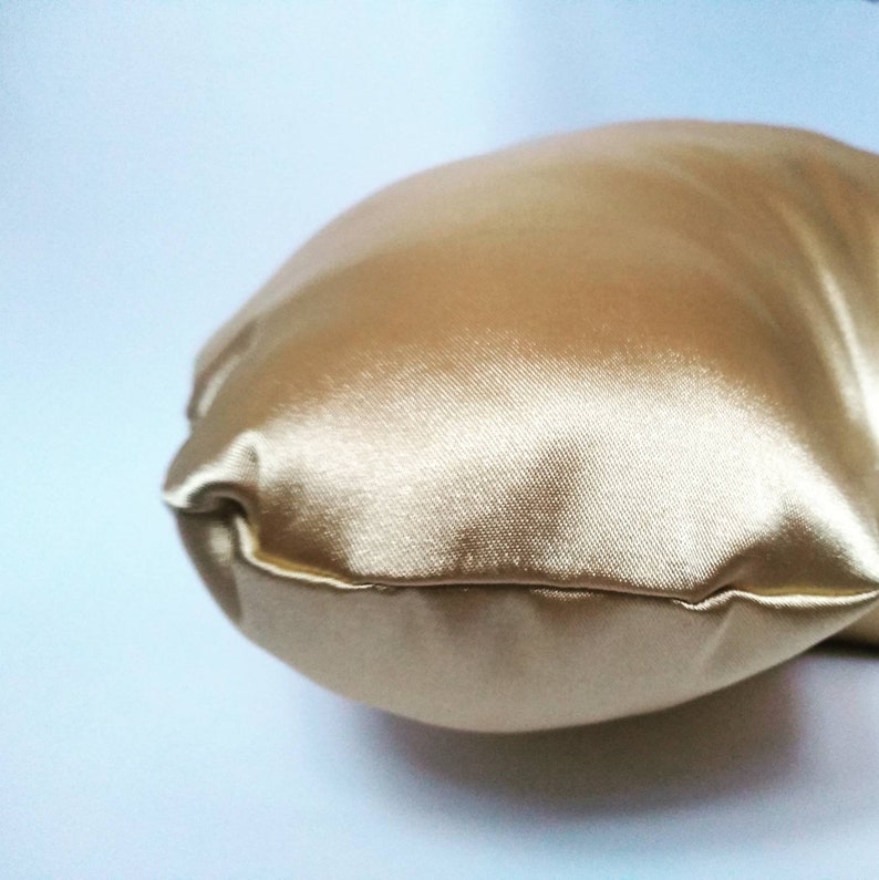 以下が含まれることがあります： 金色のサテンの枕のクローズアップ。枕は柔らかく滑らかで、上品な光沢があります。