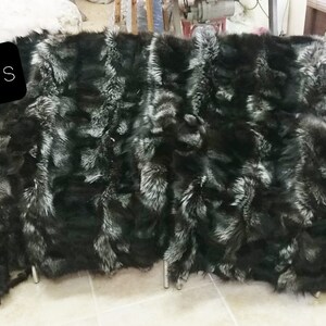 May include: A black and silver fox fur throw blanket. The fur is arranged in a striped pattern. The blanket is laid out on a tiled floor.