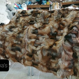 Könnte beinhalten: Eine große, braune und graue Fuchspelzdecke. Die Decke besteht aus vielen verschiedenen Fellen, die zusammengenäht wurden. Das Fell ist weich und flauschig.