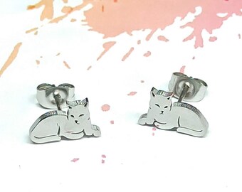 Peut inclure: Une paire de boucles d'oreilles clous en argent en forme de chat. Le chat est couché, la tête tournée sur le côté.