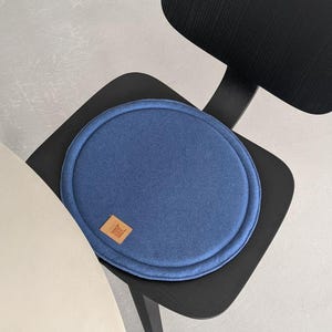 May include: A round blue chair cushion with a brown leather label. The cushion is on a black chair.