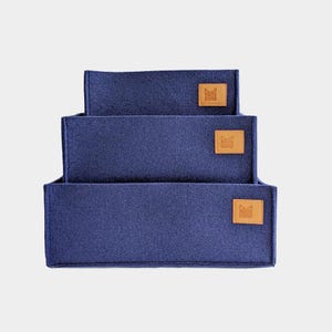 Op de afbeelding: Drie donkerblauwe opbergdozen van vilt met bruine leren etiketten waarop "Molly & Cooper" staat.