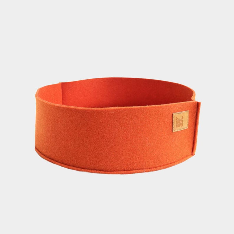 Peut inclure: Un panier pour animaux de compagnie en feutre orange de forme rectangulaire. Le lit a un design simple avec une petite &eacute;tiquette carr&eacute;e en cuir marron sur le c&ocirc;t&eacute;. Le lit est fait d'un mat&eacute;riau doux et textur&eacute;.