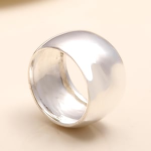 May include: A wide, polished silver band ring with a smooth, reflective surface. The ring features a thick, solid construction with a rounded exterior profile and a hollow center, showcasing a clean, metallic finish throughout the entire piece.