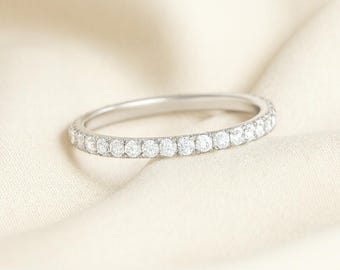 May include: A silver ring featuring a full band of small, brilliant white gemstones. The ring is displayed on a soft, cream-coloured fabric, accentuating its refined appearance. A timeless piece of jewellery.