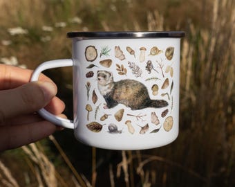 May include: A white enamel mug featuring a central illustration of a brown and cream ferret surrounded by various forest elements including mushrooms, acorns, pinecones, leaves, twigs, and small snails, finished with a dark metal rim.
