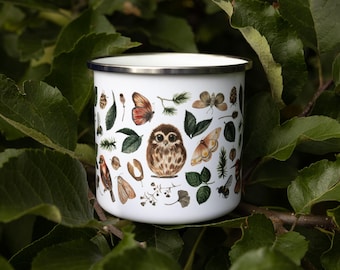 May include: A white enamel mug with a silver rim, featuring a detailed illustration of a central brown owl surrounded by various butterflies, moths, insects, green leaves, pine needles, and small twigs scattered across the exterior surface.