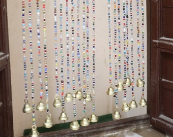 May include: A colorful beaded curtain with small bells at the bottom. The beads are in various colors, including red, blue, green, and yellow. The curtain is hanging in a doorway. The text "Pushkar Bazaar" is visible in the image.