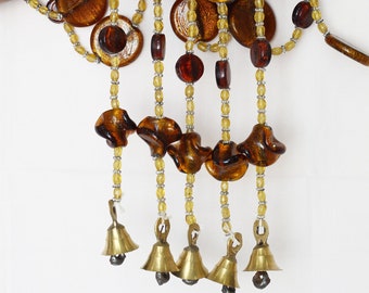 May include: A brown and gold beaded garland with glass beads and small bells. The garland is made of multiple strands of beads and has a tassel at the bottom.