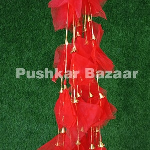 May include: A long strand of red fabric tassels with gold bells hanging from each tassel. The tassels are made of a sheer, lightweight fabric and are arranged in a cascading pattern. The bells are small and have a shiny gold finish.