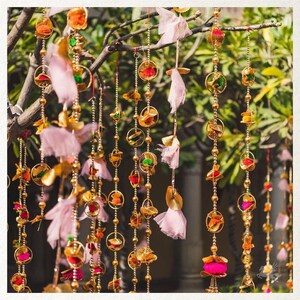 May include: A string of decorative garlands with pink, gold, and green accents. The garlands are made of fabric, beads, and metal rings. They are hanging from a tree branch.