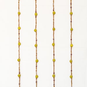 May include: Four strands of beaded garland with yellow and brown beads, each ending with a small gold bell.