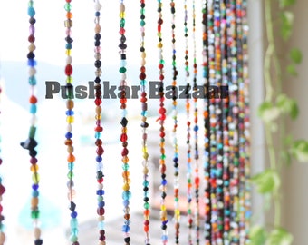 May include: A colorful beaded curtain made of glass and plastic beads in various shapes and sizes. The curtain is hanging in a window and is letting in natural light. The text "Pushkar Bazaar" is visible in the image.