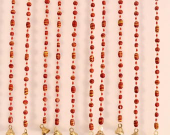 May include: A decorative beaded curtain with red and yellow beads. The beads are strung together in vertical rows, with small brass bells hanging at the bottom. The beads have a striped pattern.