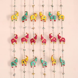 May include: A decorative hanging featuring multiple colorful elephant ornaments. The elephants are yellow, pink, and teal, with red and blue accents. Each elephant is strung on a beaded strand with decorative elements and small bells.
