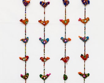 May include: Four colorful fabric bird garlands with bells at the bottom. Each garland has a string of beads and five birds in different colors, including orange, blue, green, and red.