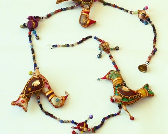 May include: A colorful beaded garland with three fabric birds. The birds are decorated with gold trim, sequins, and beads. The garland is strung with a variety of colorful beads, including red, blue, green, and gold.
