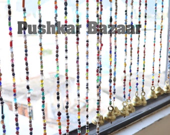 May include: A colorful beaded curtain with small bells hanging at the bottom. The beads are in various colors, including red, blue, green, and white. The curtain is hanging in a window.