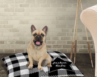 Può includere: Un letto per cani a quadri neri e bianchi di bufalo con una stella nera che presenta il testo "Jackson Rules". Un bulldog francese è seduto sul letto.