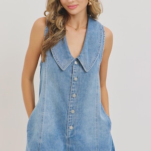May include: A sleeveless denim romper in a light blue wash. The romper features a large, rounded collar, a button-down front, and pockets. The garment is made of a soft denim material and has a relaxed fit, suitable for casual wear.