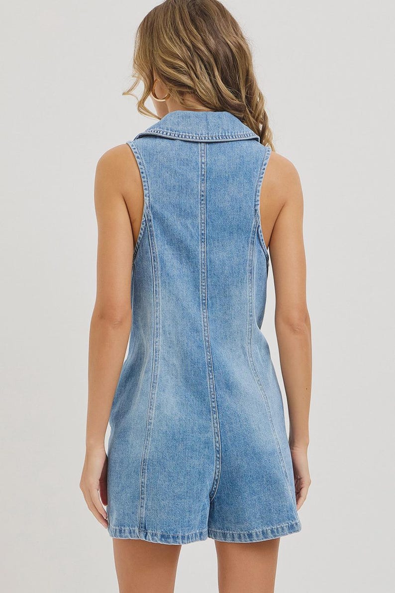 May include: Light blue denim romper with a collared neckline and sleeveless design. The romper features a button-up front and a tailored fit, showcasing a classic denim aesthetic. The shorts end at mid-thigh.