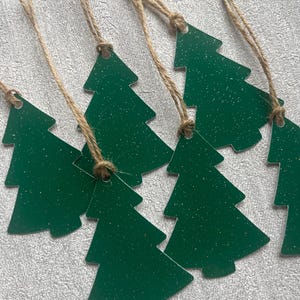 May include: Green Christmas tree-shaped decorations with glitter and twine hangers. These festive ornaments are ideal for adding a touch of holiday cheer to any Christmas tree or gift. The decorations are made of a durable material and are ready to hang.
