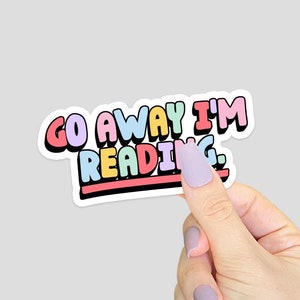 May include: A sticker with the text "Go Away I'm Reading." in rainbow colours. The sticker is on a white background.