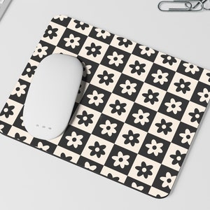 May include: A black and white checkered mouse pad with a white daisy pattern. A white wireless mouse is on the mouse pad.