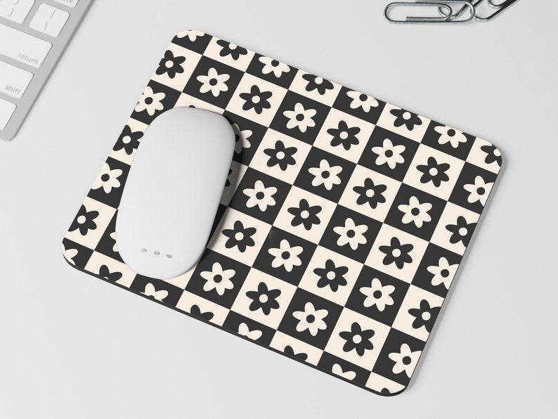 May include: A black and white checkered mouse pad with a white daisy pattern. A white wireless mouse is on the mouse pad.