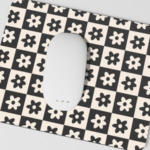 May include: A white mouse pad with a black and white checkered pattern featuring stylized black flowers. The mouse pad is designed to be used with a computer mouse.