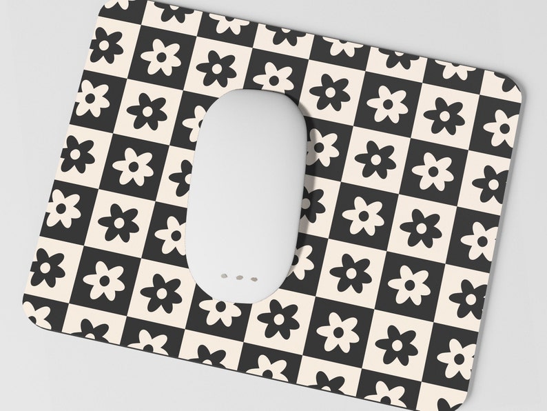 May include: A white mouse pad with a black and white checkered pattern featuring stylized black flowers. The mouse pad is designed to be used with a computer mouse.